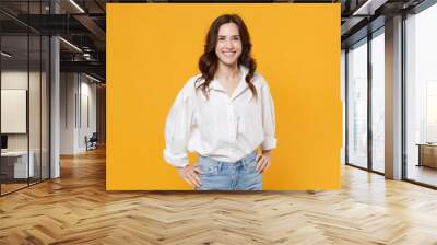 Smiling young brunette business woman in white shirt posing isolated on yellow background studio portrait. Achievement career wealth business concept. Mock up copy space. Standing with arms akimbo. Wall mural