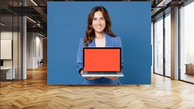 Smiling young brunette woman 20s wearing basic jacket hold laptop pc computer with blank empty screen mock up copy space looking camera isolated on bright blue colour wall background studio portrait. Wall mural