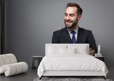 Smiling young business man in classic black suit shirt tie posing isolated on grey background. Achievement career wealth business concept. Mock up copy space. Holding hands crossed, looking aside. Wall mural