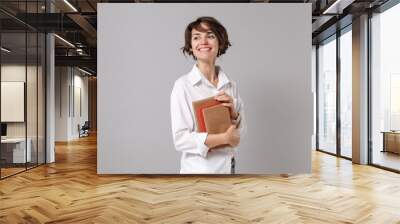 Smiling young business woman in white shirt posing isolated on grey background studio portrait. Achievement career wealth business concept. Mock up copy space. Holding books, notebooks, looking aside. Wall mural