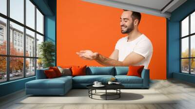 Smiling young man in casual white t-shirt posing isolated on bright orange wall background studio portrait. People sincere emotions lifestyle concept. Mock up copy space. Holding something in hands. Wall mural