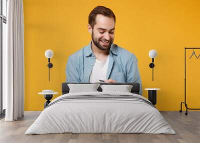 Smiling young student man in casual blue shirt posing isolated on yellow orange background, studio portrait. People sincere emotions lifestyle concept. Mock up copy space. Writing note in notebook. Wall mural