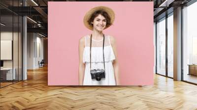 Smiling young tourist woman in summer dress, hat with photo camera on neck isolated on pink background. Female traveling abroad to travel weekends getaway. Air flight journey concept. Looking camera. Wall mural