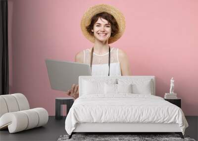 Smiling young tourist woman in summer dress hat with photo camera isolated on pink background. Female traveling to travel weekends getaway. Air flight journey concept. Working on laptop pc computer. Wall mural