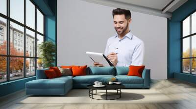 Smiling young unshaven business man in light shirt posing isolated on grey background. Achievement career wealth business concept. Mock up copy space. Hold clipboard with papers document write notes. Wall mural