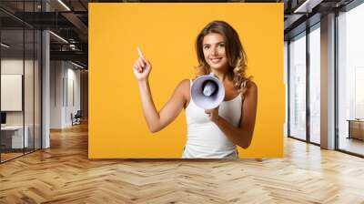 Smiling young woman girl in light casual clothes posing isolated on yellow orange background, studio portrait. People lifestyle concept. Mock up copy space. Scream in megaphone, point index finger up. Wall mural