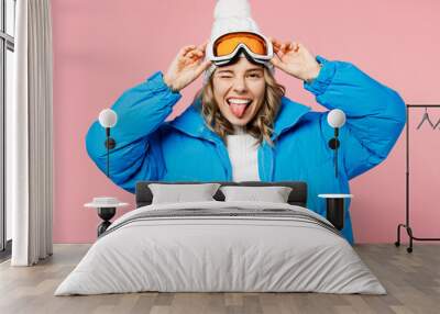 Snowboarder fun woman wear blue suit hat ski padded jacket hold take off goggles mask show tongue wink isolated on plain pastel pink background. Winter extreme sport hobby weekend trip relax concept. Wall mural