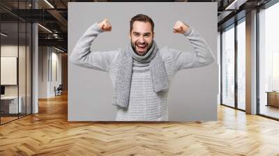 Strong young man in gray sweater, scarf posing isolated on grey background studio portrait. Healthy fashion lifestyle, people emotions, cold season concept. Mock up copy space. Showing biceps muscles. Wall mural