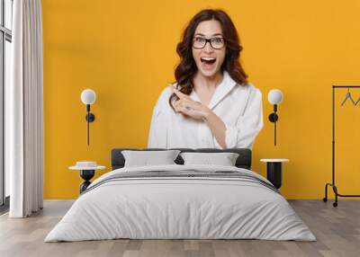 Surprised young brunette business woman in white shirt glasses isolated on yellow background studio portrait. Achievement career wealth business concept. Mock up copy space. Point index finger aside. Wall mural