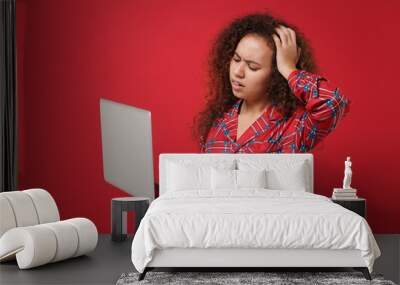 Tired young african american girl in pajamas homewear resting at home isolated on red background. Relax good mood lifestyle concept. Mock up copy space. Work on laptop pc computer put hand on head. Wall mural