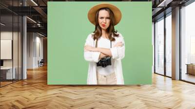 Traveler frowning sad tourist woman in casual clothes hat camera on neck hold hands crossed folded isolated on green background Passenger travel abroad on weekends getaway. Air flight journey concept. Wall mural