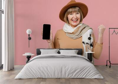 Traveler tourist winner elderly woman 55 years old wear brown shirt hat scarf hold use mobile cell phone with blank screen workspace area isolated plain pastel light pink background studio portrait Wall mural