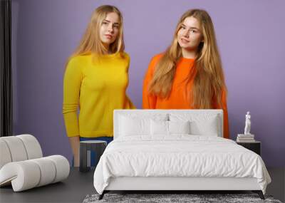 Two young blonde twins sisters girls in vivid colorful clothes standing, looking camera isolated on pastel violet blue wall background in studio. People family lifestyle concept. Mock up copy space. Wall mural