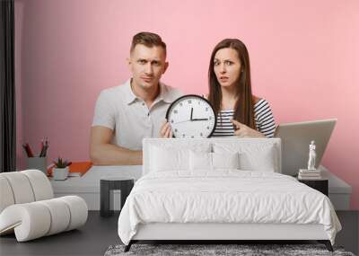 Two young fun shocked business woman man colleagues sit work at white desk with clock, laptop isolated on pastel pink background. Achievement career concept. Copy space advertising, youth co working. Wall mural