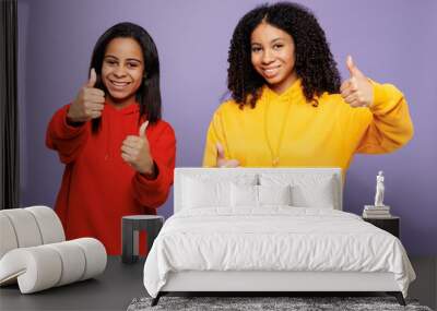 Two young happy little kid teen girls women they wear red yellow hoodie casual clothes showing thumb up like gesture looking camera isolated on plain pastel light purple background. Lifestyle concept. Wall mural