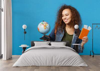 Young african american girl teen student in denim clothes, backpack hold pass isolated on blue wall background studio portrait. Education in high school university college concept. Mock up copy space. Wall mural