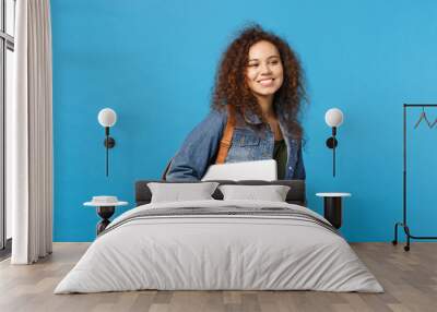 Young african american girl teen student in denim clothes, backpack hold pc isolated on blue wall background studio portrait. Education in high school university college concept. Mock up copy space. Wall mural