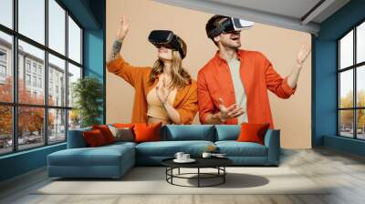 Young amazed caucasian happy couple two friends family man woman wear casual clothes together watching in vr headset pc gadget isolated on pastel plain light beige color background studio portrait. Wall mural