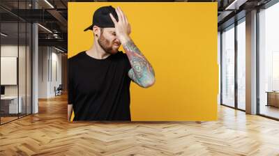 Young bearded tattooed man 20s he wearing casual black t-shirt cap put hand on face facepalm epic fail mistaken omg gesture isolated on plain yellow wall background studio. People lifestyle concept. Wall mural