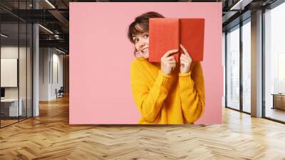 Young brunette woman girl in yellow sweater posing isolated on pink wall background studio portrait. People sincere emotions lifestyle concept. Mock up copy space. Holding and covering face with book. Wall mural