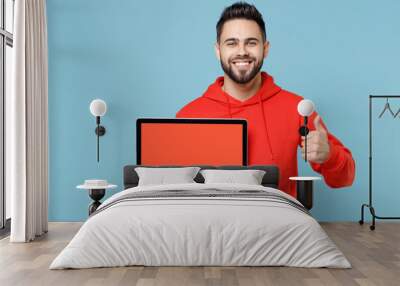 Young caucasian smiling web designer bearded man 20s in casual red orange hoodie hold laptop pc computer, blank screen workspace area show thumb up gesture isolated on blue background studio portrait. Wall mural