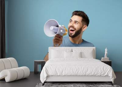 Young cheerful funny man in casual clothes posing isolated on blue wall background, studio portrait. People sincere emotions lifestyle concept. Mock up copy space. Scream in megaphone, looking aside. Wall mural