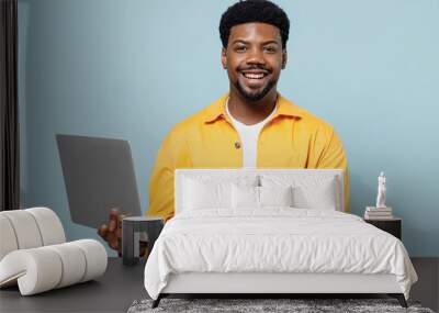 Young cheerful happy man of African American ethnicity 20s in yellow shirt hold use work on laptop pc computer isolated on plain pastel light blue background studio portrait. People lifestyle concept. Wall mural