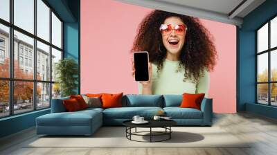 Young curly latin woman 20s years old wears mint t-shirt sunglasses hold in hand use mobile cell phone with blank screen workspace area isolated on plain pastel light pink background studio portrait. Wall mural