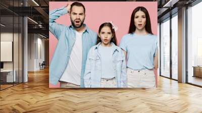 Young disappointed parents mom dad with child kid daughter teen girl in blue clothes spread hands scratch hold head isolated on plain pastel pink background. Family day parenthood childhood concept. Wall mural