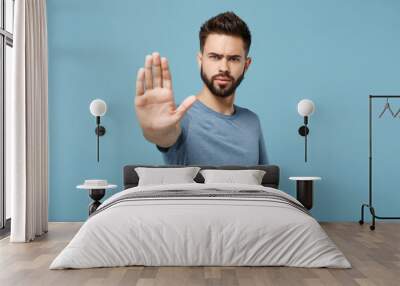 Young displeased serious man in casual clothes posing isolated on blue wall background, studio portrait. People sincere emotions lifestyle concept. Mock up copy space. Showing stop gesture with palm. Wall mural