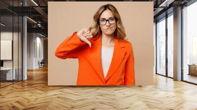 Young dissatisfied sad employee business woman corporate lawyer 30s wear classic formal orange suit glasses work in office showing thumb down dislike gesture isolated on plain beige background studio. Wall mural