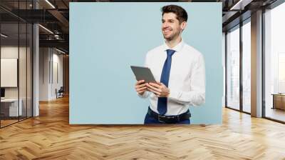 Young employee IT business man corporate lawyer wears classic formal shirt tie work in office hold use digital tablet pc computer look aside isolated on plain pastel blue background studio portrait. Wall mural