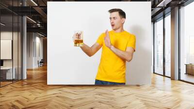 Young European serious handsome man in yellow t-shirt refuse pint mug of beer, show stop drink alcohol gesture with hand isolated on white background. Sport teenager health, healthy lifestyle concept. Wall mural