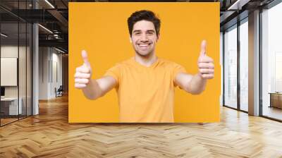 Young excited satisfied unshaved caucasian smiling man 20s years old wearing casual basic blank print design t-shirt showing thumbs up like gesture isolated on yellow color background studio portrait. Wall mural