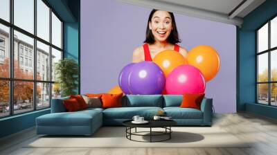 Young excited woman of Asian ethnicity she wear casual clothes red tank shirt hold bunch of colorful air balloons isolated on plain pastel light purple background studio portrait. Lifestyle concept. Wall mural