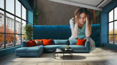 Young frustrated ill woman she 20s wear casual clothes mint t-shirt holding head suffer from headache close eyes sit on blue sofa indoor rest at home in own room apartment. People lifestyle concept Wall mural