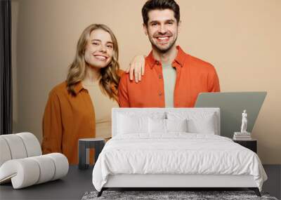 Young fun couple two friends family IT man woman wear casual clothes looking camera hold use work on laptop pc computer together isolated on pastel plain light beige color background studio portrait. Wall mural