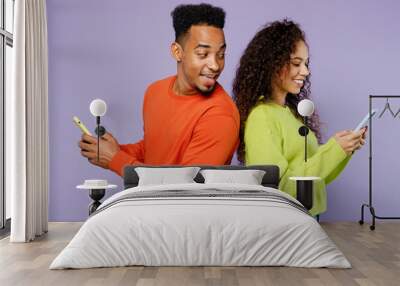 Young fun couple two friends family man woman of African American ethnicity wear casual clothes together hold use mobile cell phone stand back to back peep isolated on plain light purple background. Wall mural