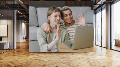 Young fun couple two gay IT men wear casual clothes hold use work on laptop pc computer sit on sofa couch home hotel flat rest spend free time in living room. Pride day june month love lgbtq concept. Wall mural