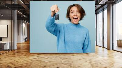 Young fun excited woman wear knitted sweater look camera hold in hand giving car key fob keyless system isolated on plain pastel light blue cyan background studio portrait. People lifestyle concept. Wall mural