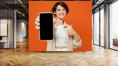 Young fun happy woman she wear beige shirt casual clothes hold in hand use blank screen workspace area mobile cell phone show thumb up isolated on plain orange red background studio Lifestyle concept Wall mural