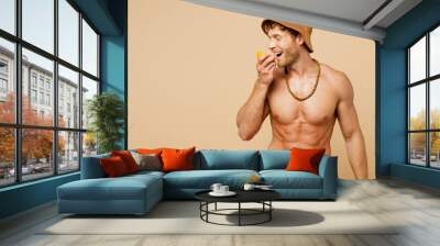 Young fun sexy man wear yellow shorts swimsuit hat relax rest near hotel pool biting eat half of orange fruit isolated on plain pastel light beige background. Summer hot vacation sea sun tan concept. Wall mural