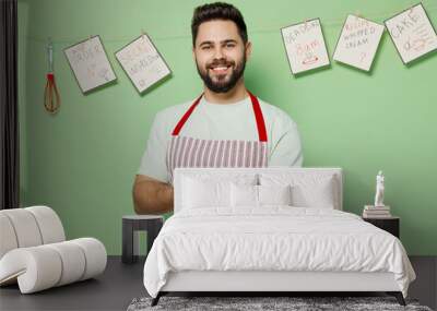 Young fun smiling happy male chef confectioner baker man 20s in striped apron hold point hand on warm homemade bread look camera isolated on plain pastel light green background. Cooking food concept Wall mural