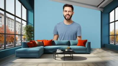 Young funny cheerful handsome man in casual clothes posing isolated on blue wall background, studio portrait. People sincere emotions lifestyle concept. Mock up copy space. Blinking, showing tongue. Wall mural