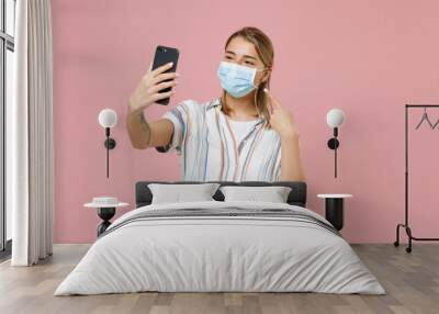 Young girl in casual striped shirt isolated on pink background. Epidemic pandemic coronavirus 2019-ncov sars covid-19 flu virus concept Doing selfie shot on mobile phone pointing on sterile face mask. Wall mural