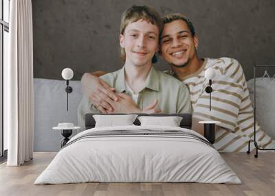 Young happy calm couple two gay men wear casual clothes together hugging look camera sit on sofa couch at home flat rest spend free spare time in living room. Pride day june month love lgbtq concept. Wall mural