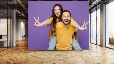 Young happy cool couple two friends family man woman together wear yellow casual clothes giving piggyback ride to joyful, sit on back show v-sign isolated on plain violet background studio portrait Wall mural