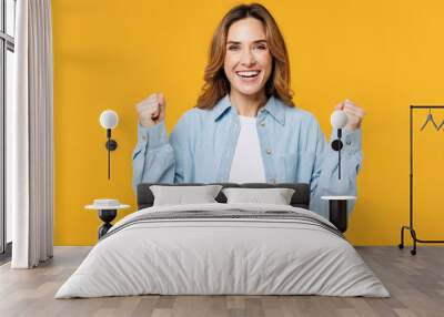 Young happy cool woman she wear blue shirt white t-shirt casual clothes doing winner gesture celebrate clenching fists say yes isolated on plain yellow background studio portrait. Lifestyle concept. Wall mural