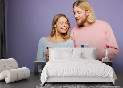 Young happy couple two friends family man woman wear pink blue casual clothes together hold in hand use looking at mobile cell phone isolated on pastel plain light purple background studio portrait. Wall mural