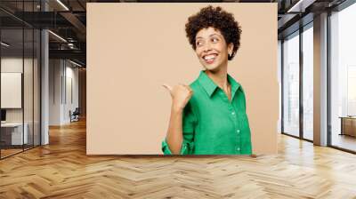 Young happy fun woman of African American ethnicity wear green shirt casual clothes point thumb finger aside indicate on area isolated on plain pastel light beige background studio. Lifestyle concept. Wall mural